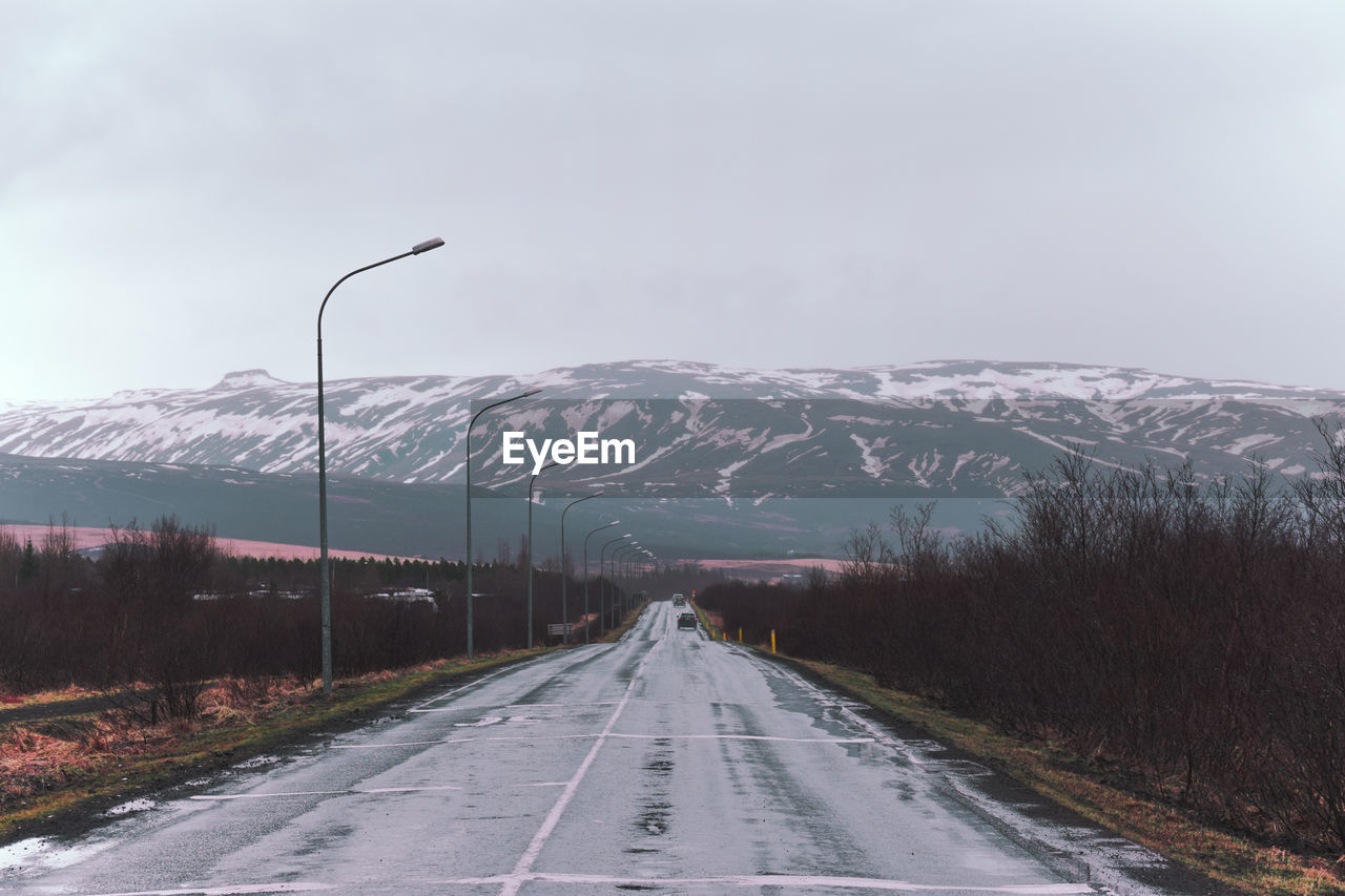 Diminishing perspective of road leading towards snowcapped mountains against sky