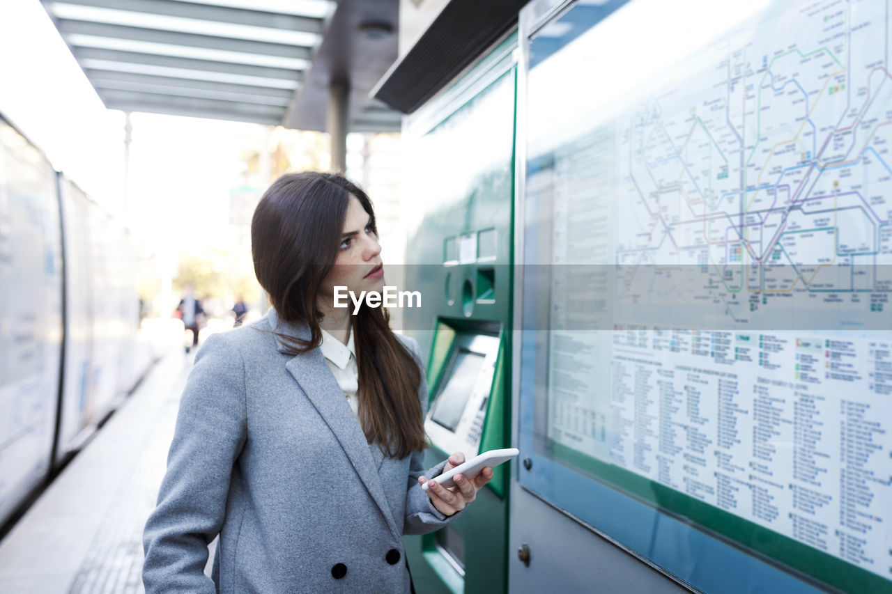 Spain, barcelona, young woman with smartphone looking at map at station