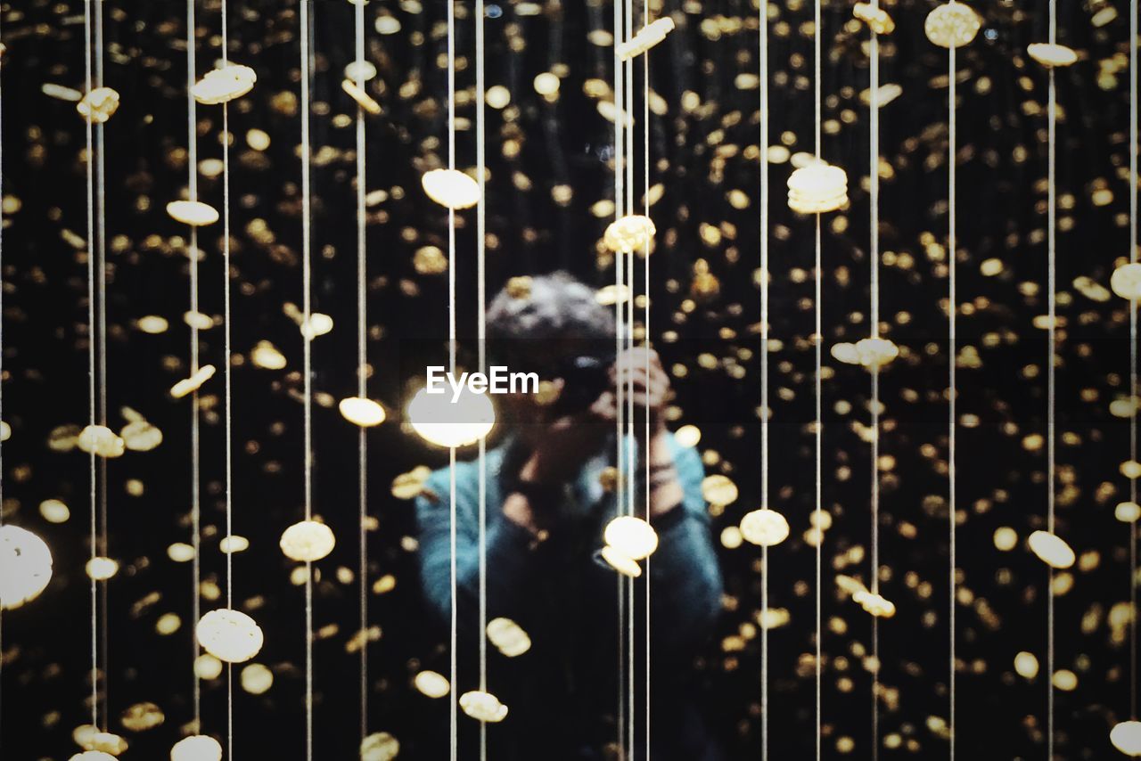 Woman photographing while standing amidst illuminated lights at night