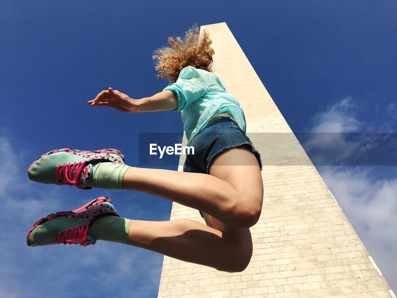 Low angle view of young woman jumping by building against sky