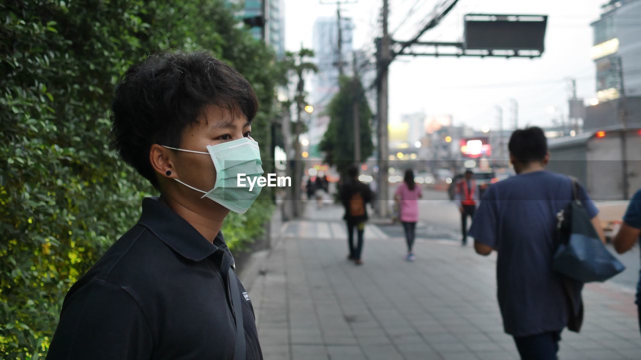 Man wearing pollution mask standing on sidewalk in city