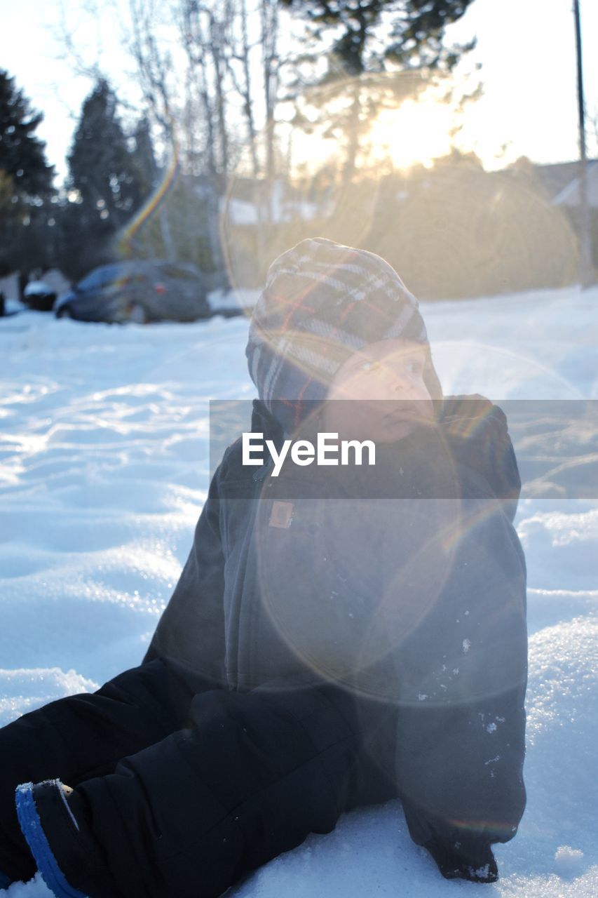 Cute baby boy sitting on snow covered field