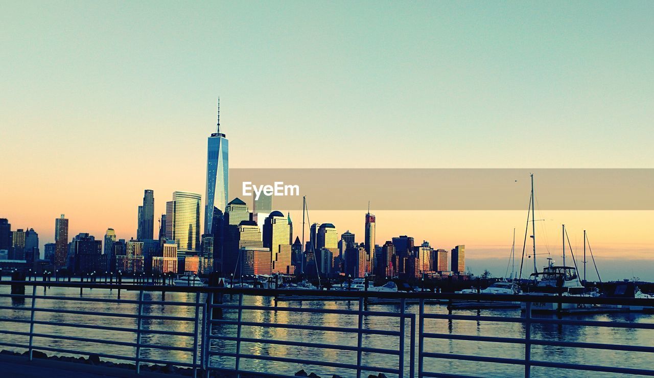 Cityscape by river against clear sky at sunset