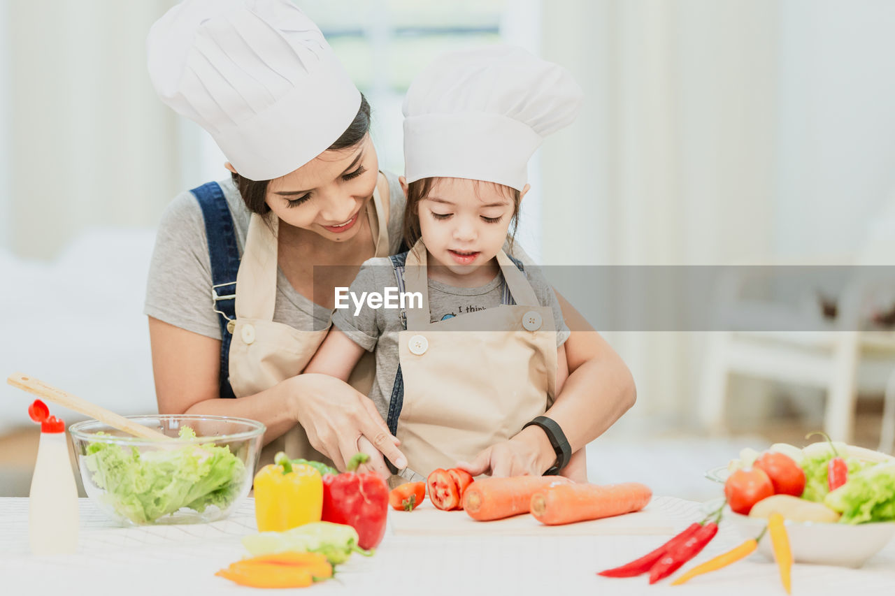 FULL LENGTH OF MOTHER AND DAUGHTER IN KITCHEN AT HOME