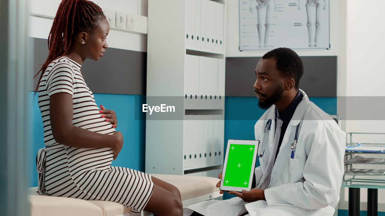 Doctor holding digital tablet while discussing with patient