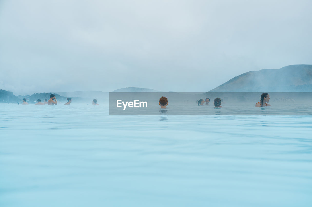 PEOPLE SWIMMING IN WATER AGAINST SKY