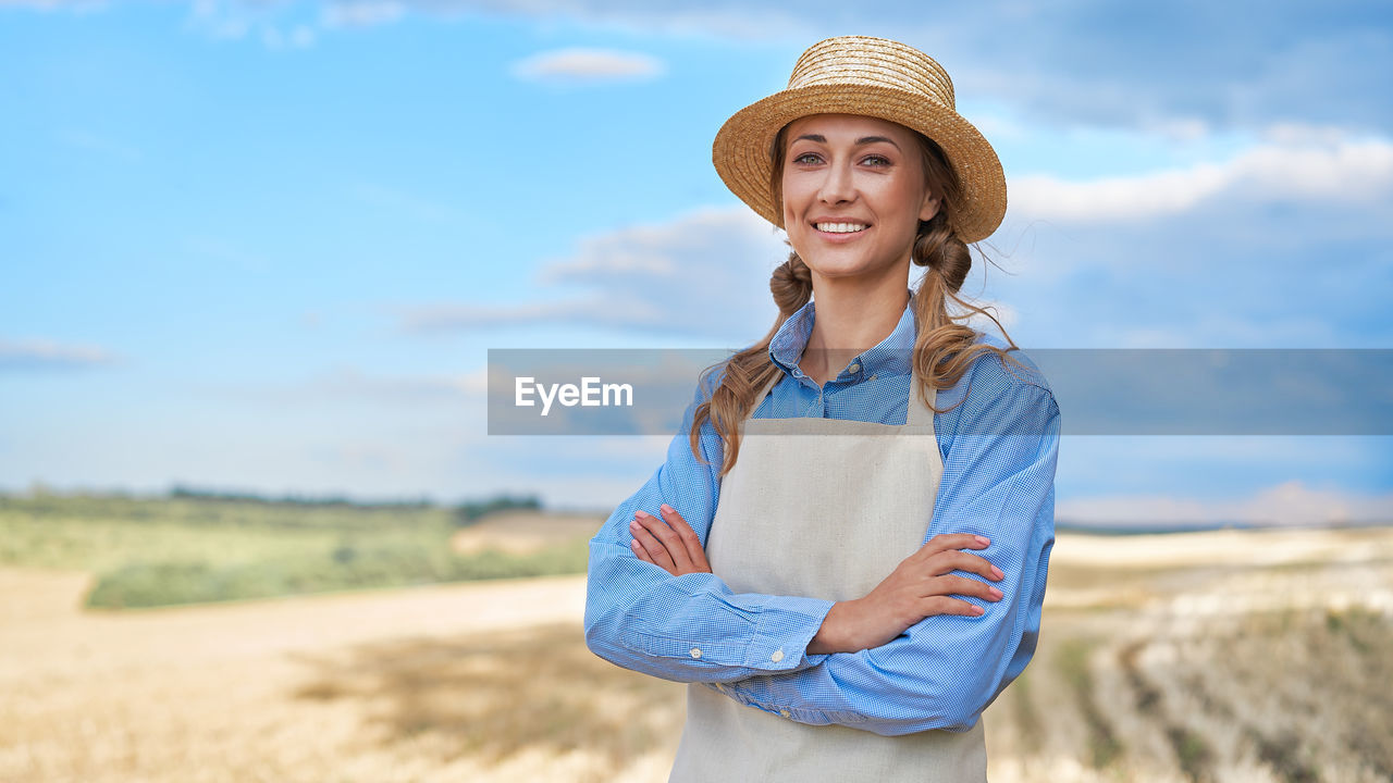 PORTRAIT OF SMILING YOUNG WOMAN STANDING IN FIELD