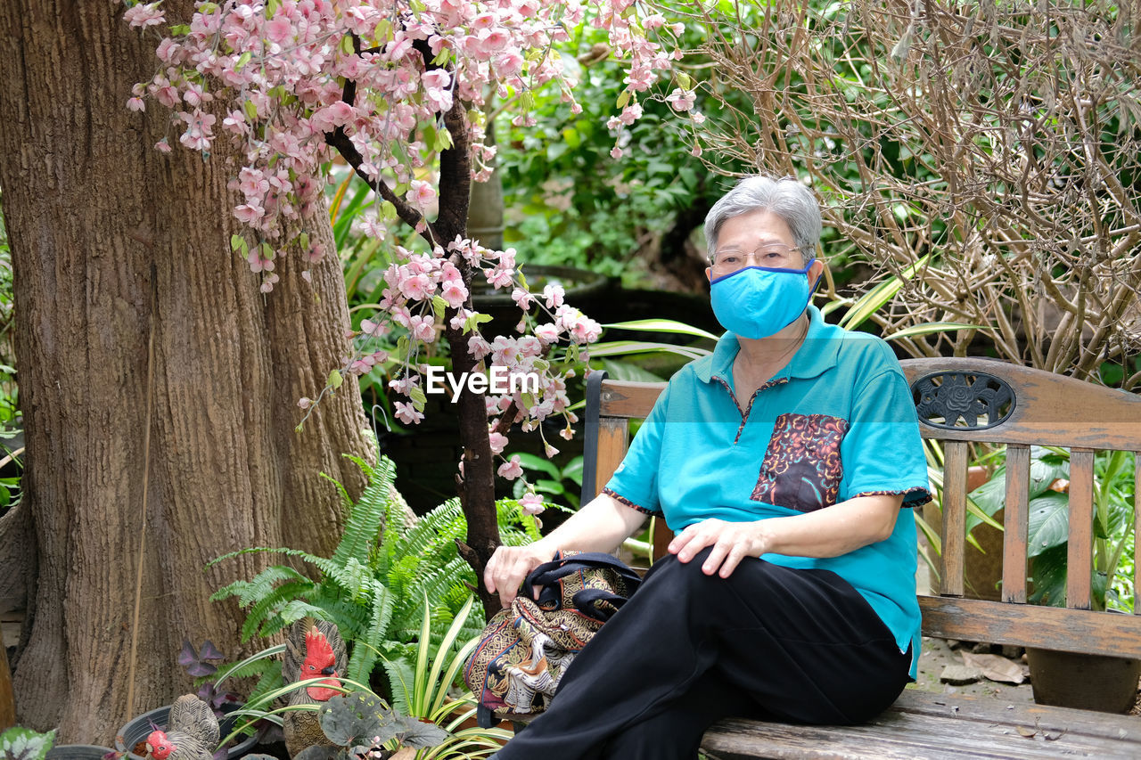 Portrait of woman wearing mask sitting by potted plant outdoors