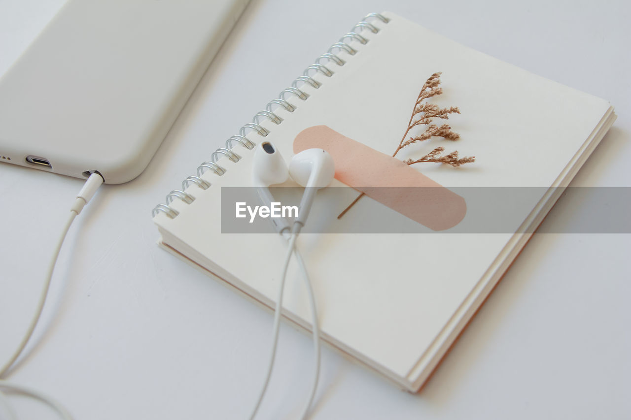 High angle view of earphones with book and smart phone over white background