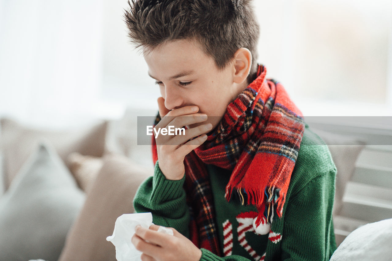Close-up of boy sneezing at home