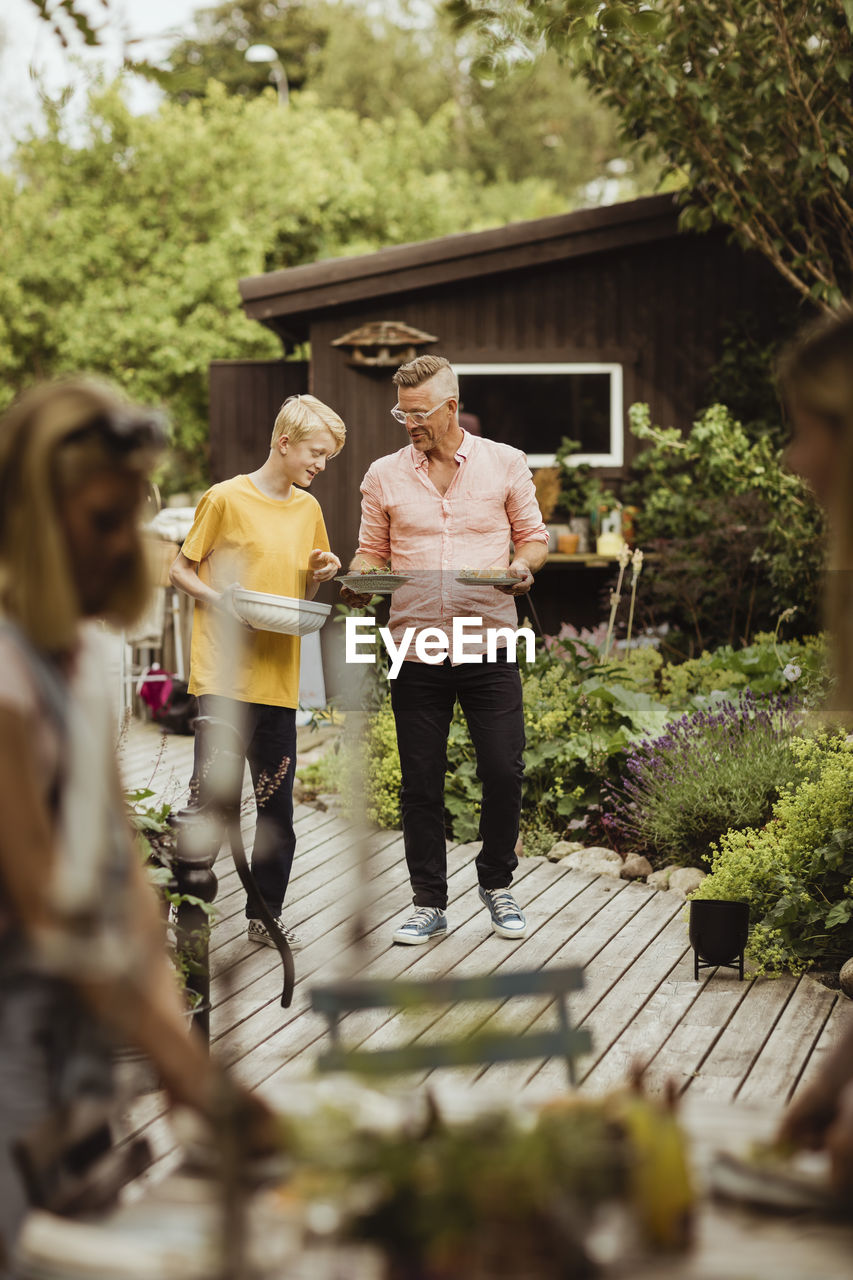 Father and son walking with bowl and plate in back yard during social event