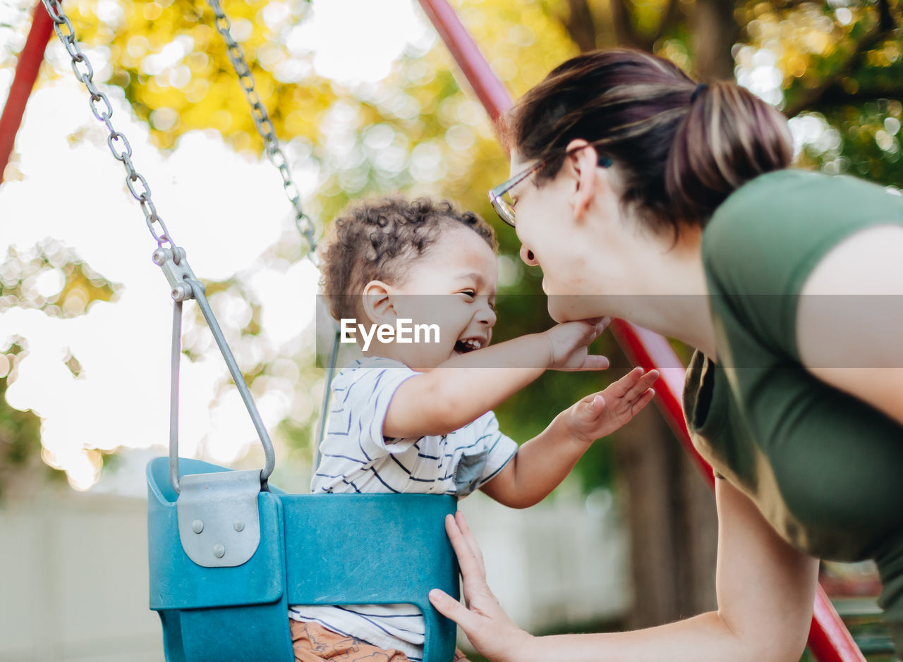 Young millennial mother and diverse mixed race toddler boy at park on nice summer day having fun