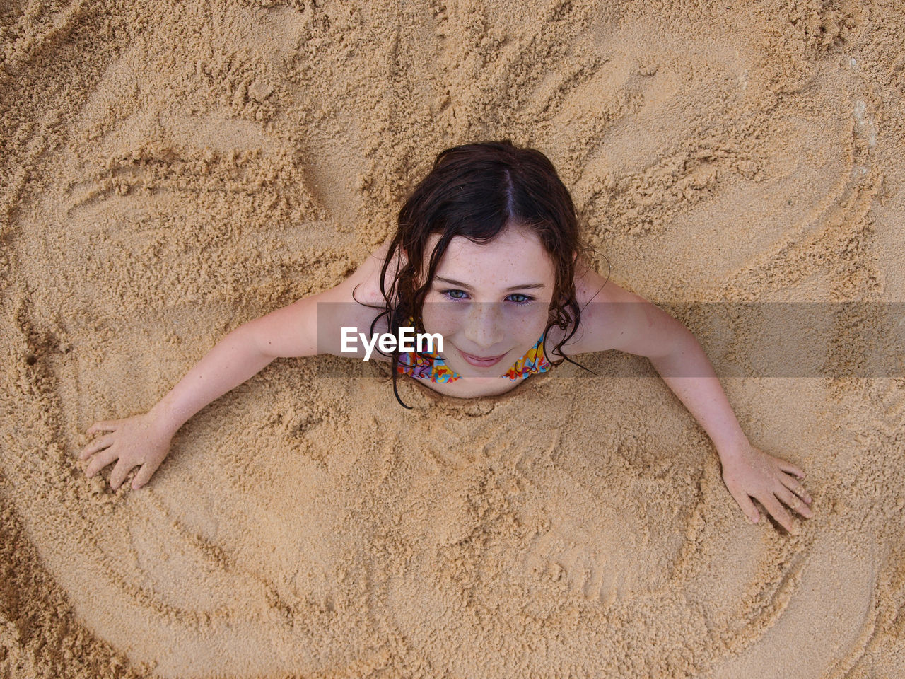 High angle portrait of playful girl buried in sand at beach