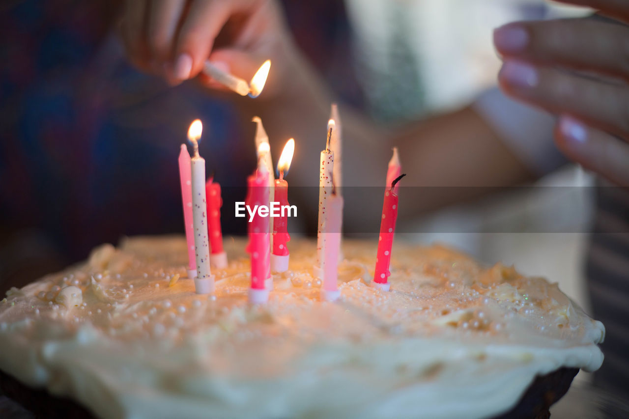 Close-up of hand igniting candles on birthday cake at table