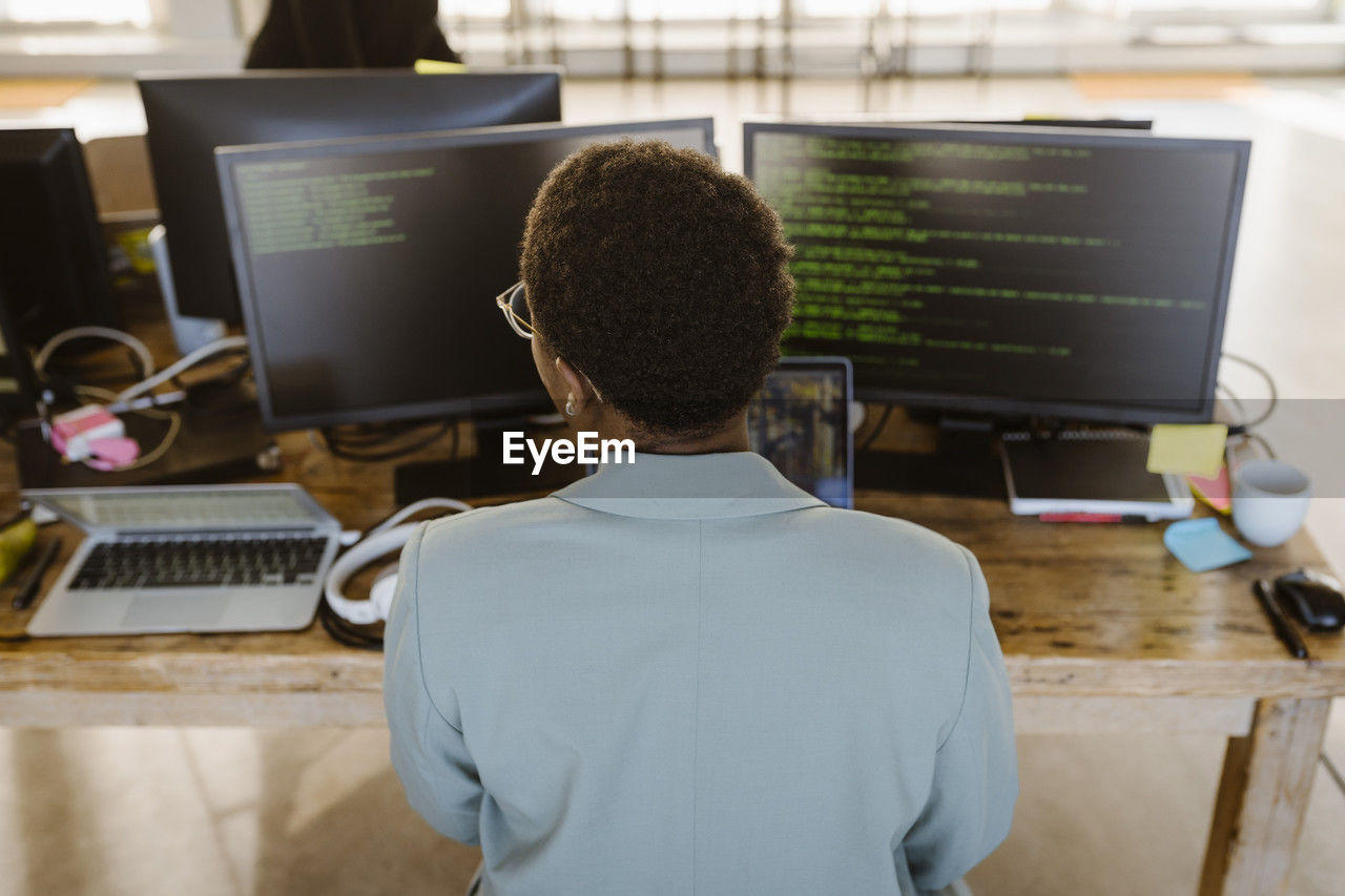 Rear view of female programmer working on computer at desk in creative office