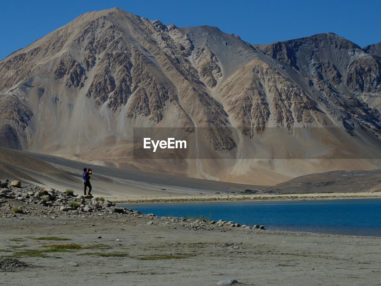 Mid distant view of man standing by pangong tso lake against mountains