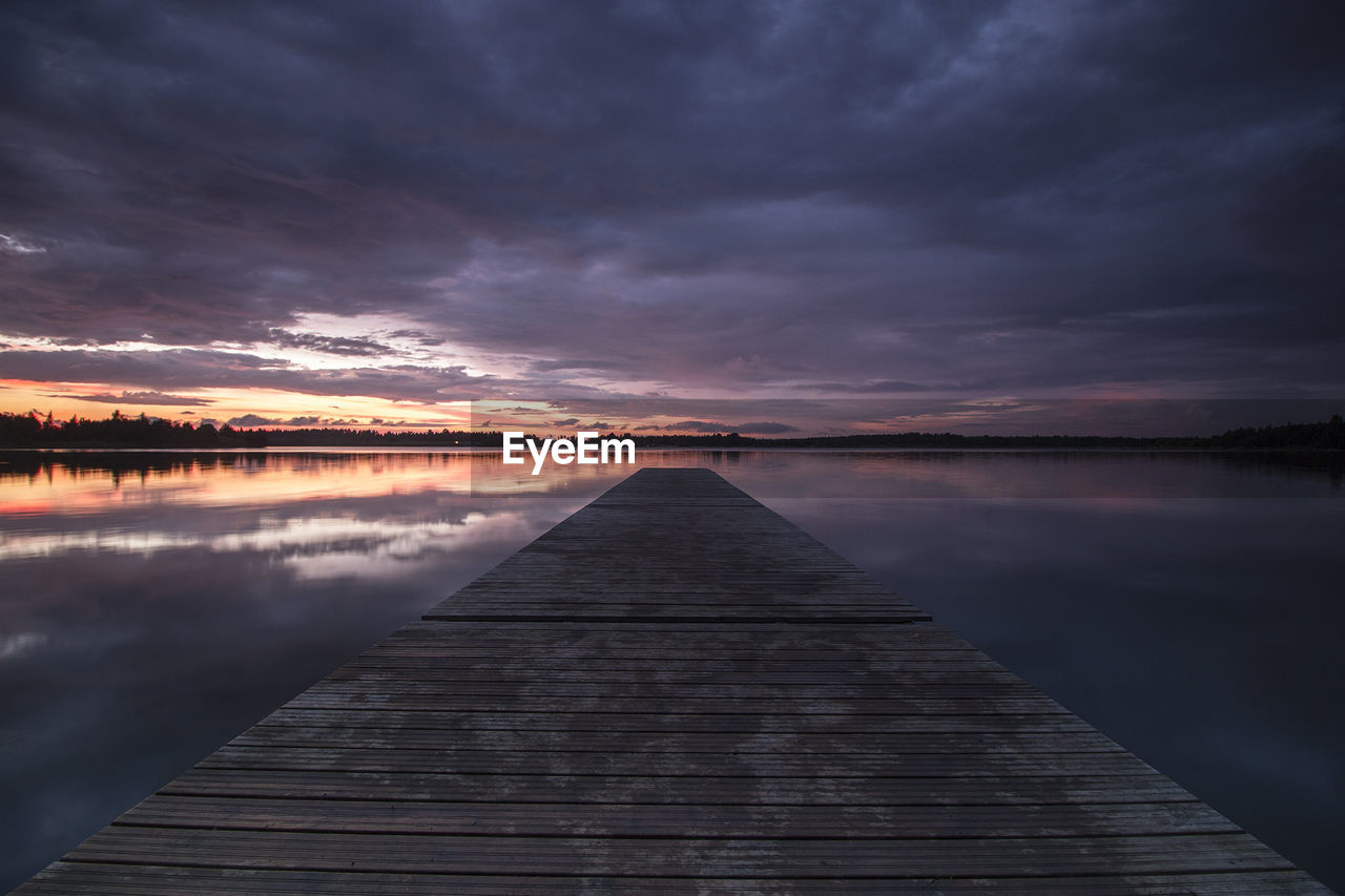Jetty over lake against cloudy sky during sunset