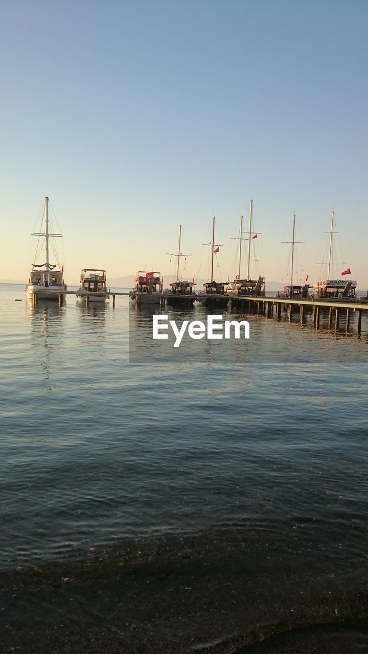 Sailboats moored on sea against clear sky