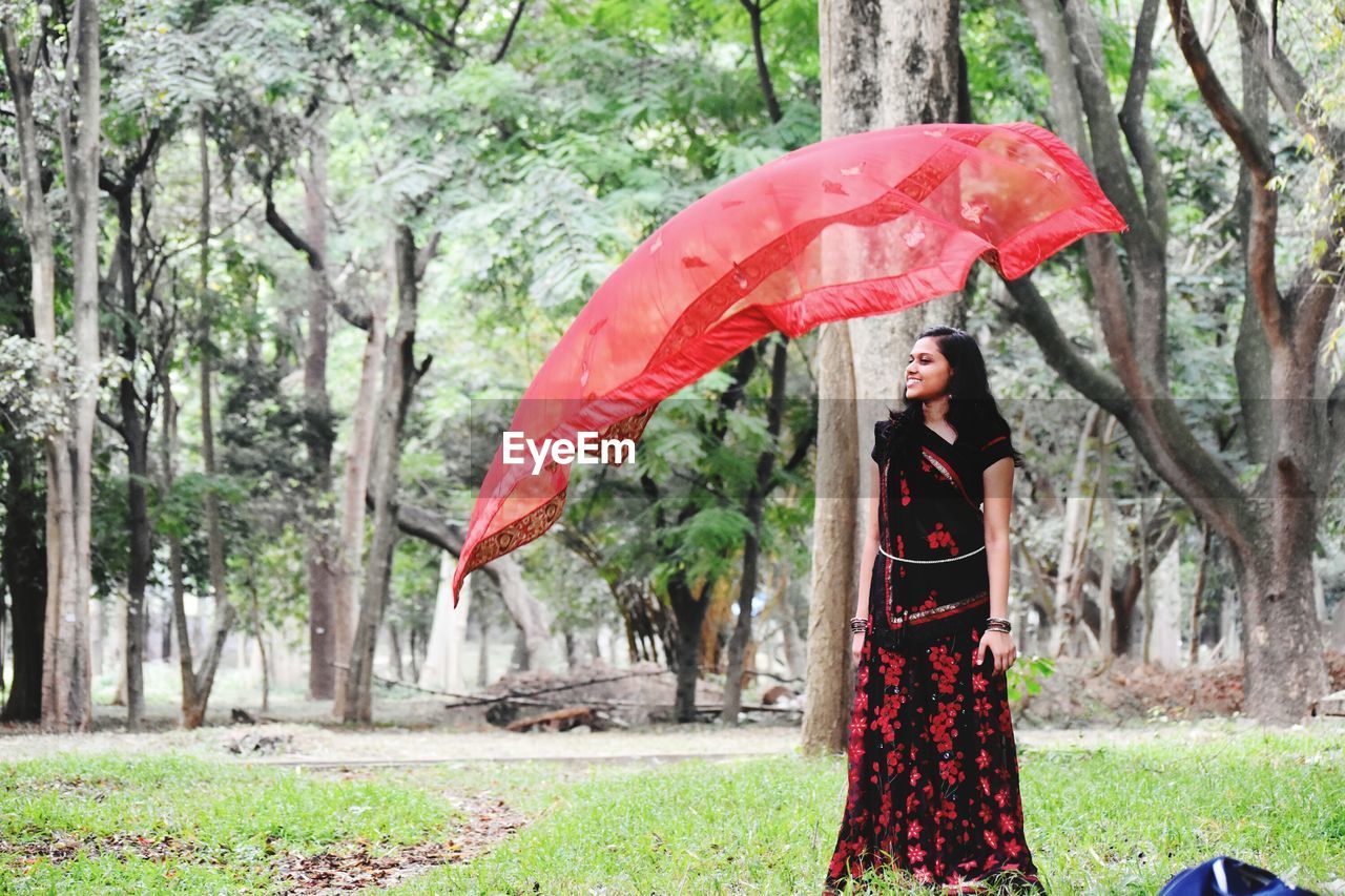 Young woman wearing traditional clothing while looking at dupatta flying in air at park