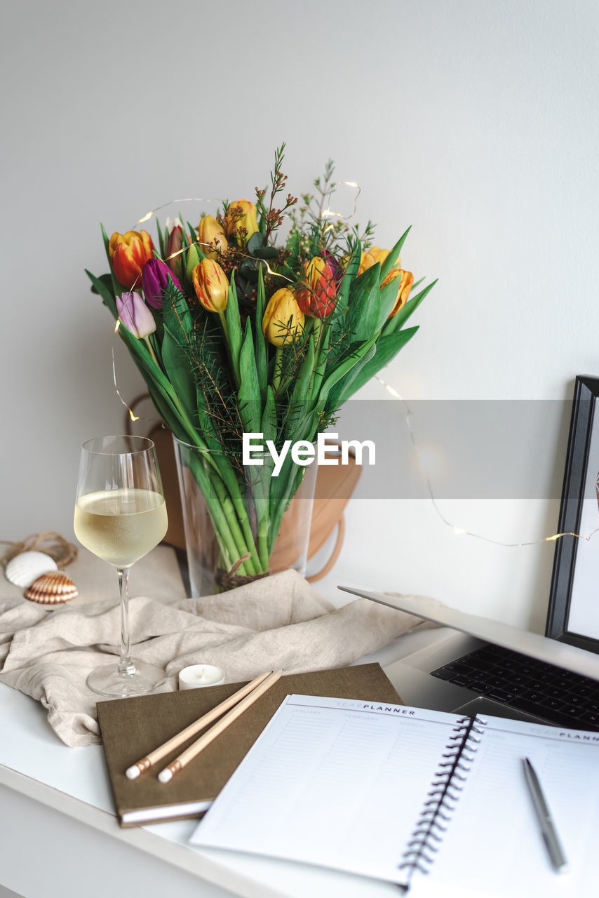 Still life with a bouquet of colorful spring tulips and a glass of white wine on the work desk.