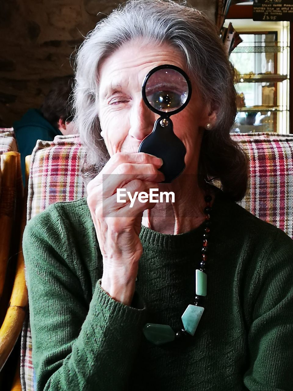 Portrait of senior woman holding magnifying glass at home