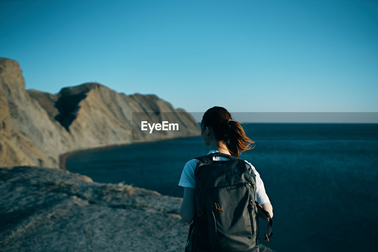 REAR VIEW OF WOMAN LOOKING AT SEA AGAINST SKY