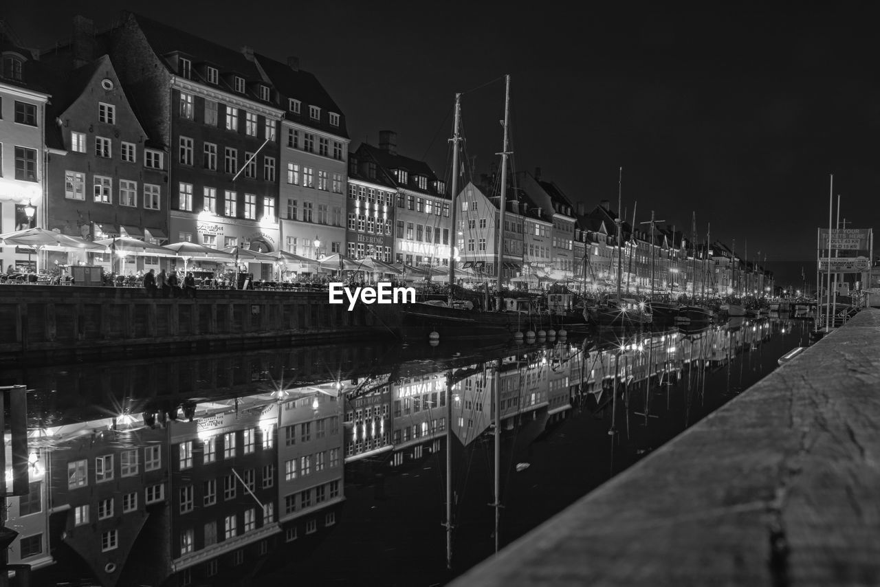 Illuminated buildings by canal against sky in city at night