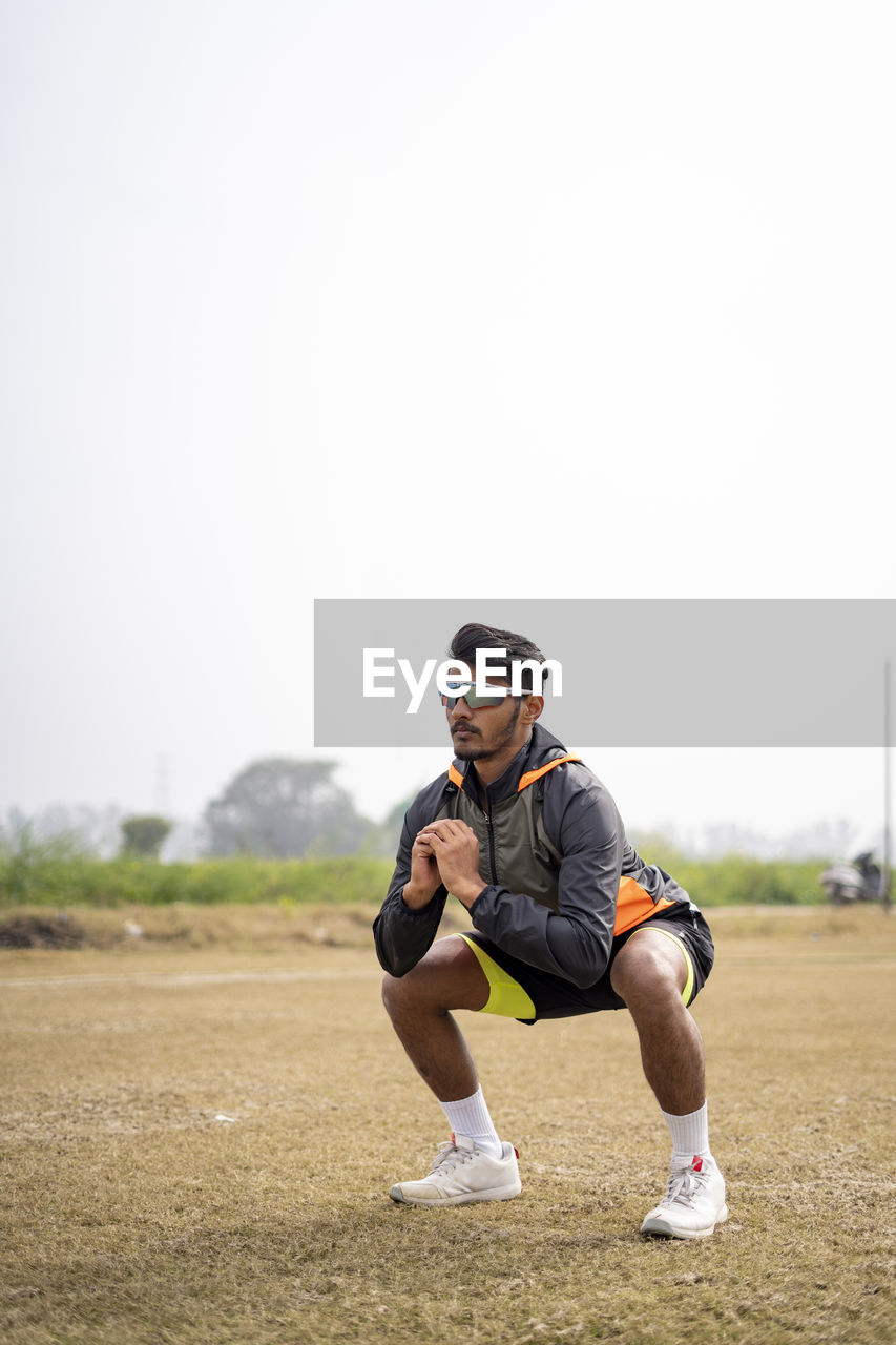 Young indian sports man doing squats in the field. sports and healthy lifestyle concept.