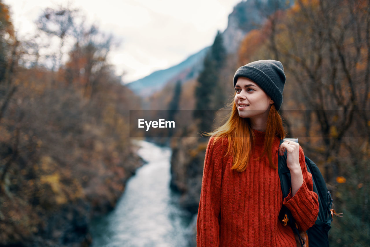 BEAUTIFUL YOUNG WOMAN STANDING AGAINST TREE DURING WINTER