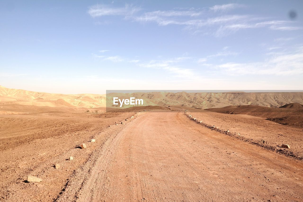 Dirt road in desert against sky