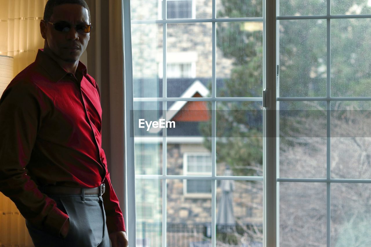 Portrait of man standing by window at home