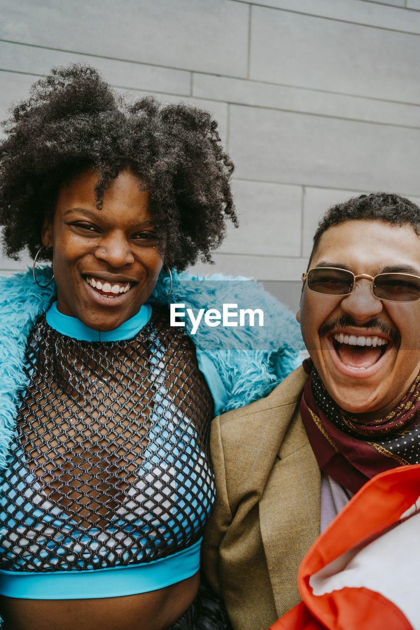 Cheerful hipster woman and gay man against wall