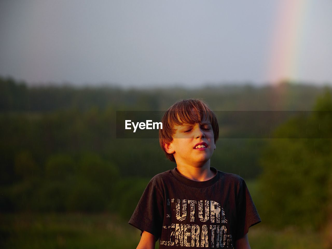 Boy with eyes closed standing against trees during sunset