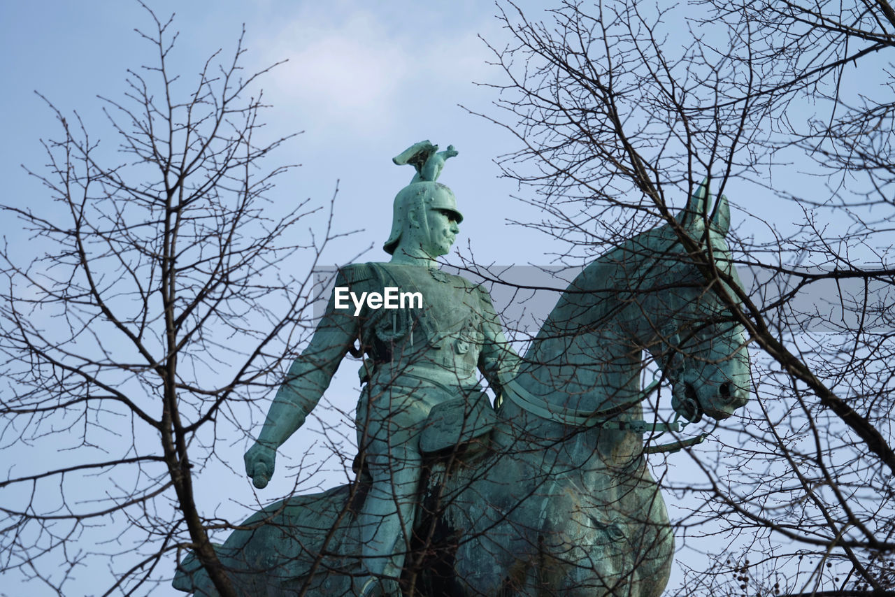 Low angle view of statue seen through bare trees against sky