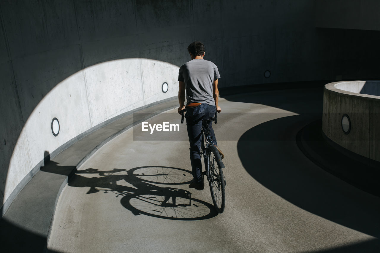 REAR VIEW OF MAN RIDING BICYCLE ON ROAD