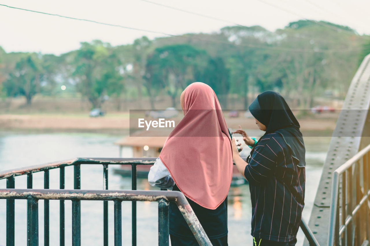 REAR VIEW OF COUPLE STANDING ON RAILING