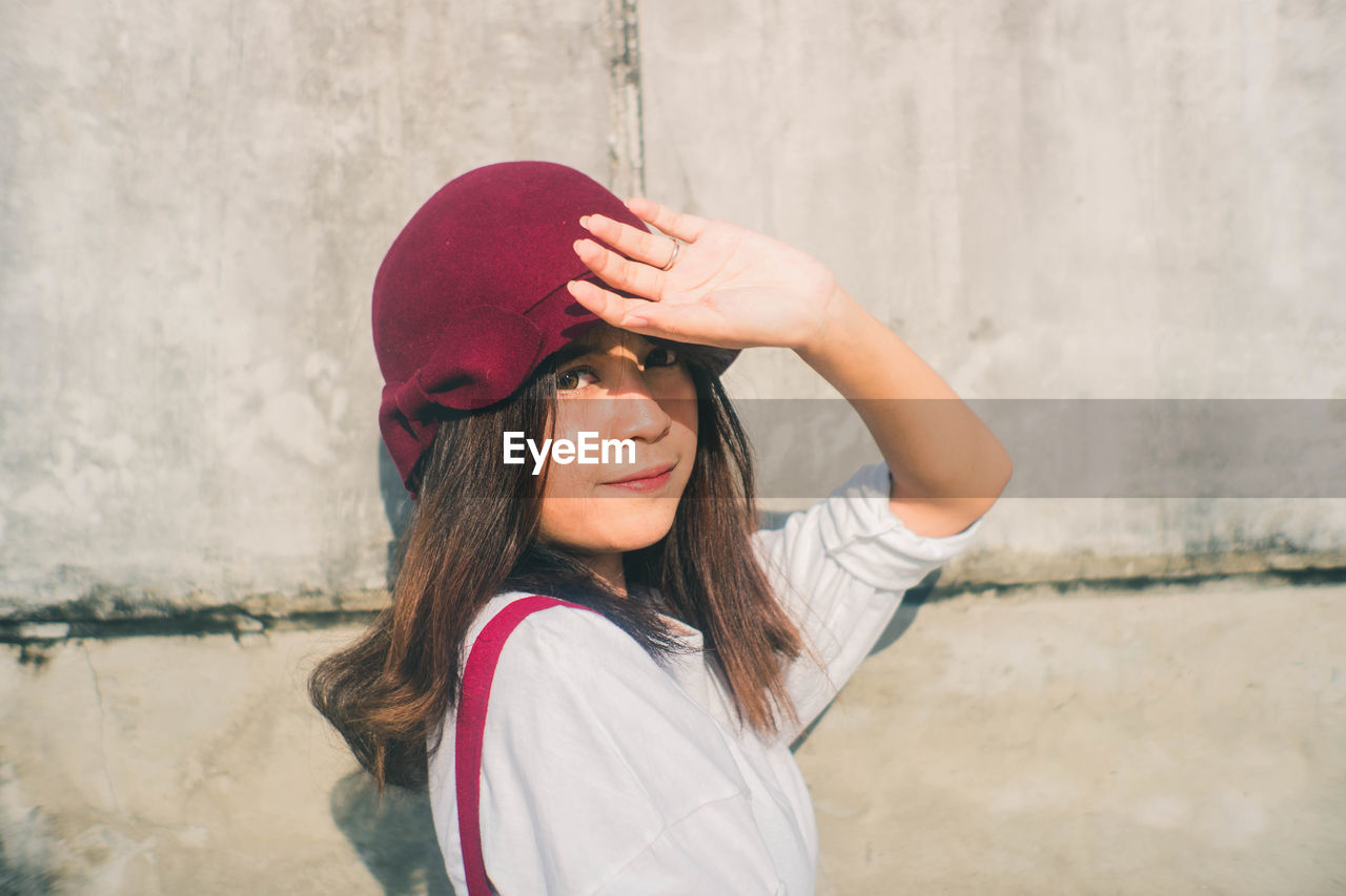 Portrait of young woman shielding eyes against wall