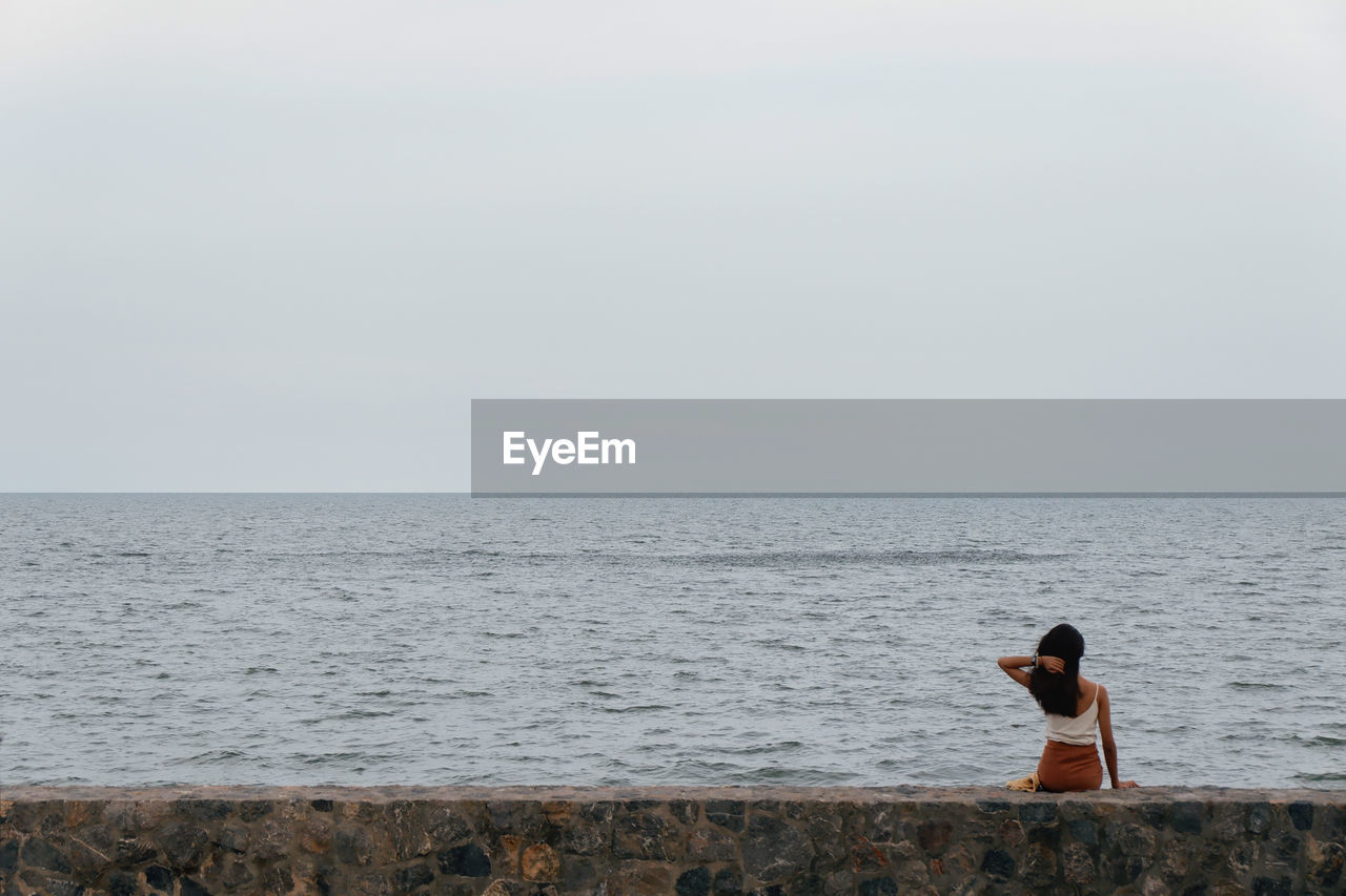 REAR VIEW OF MAN LOOKING AT SEA