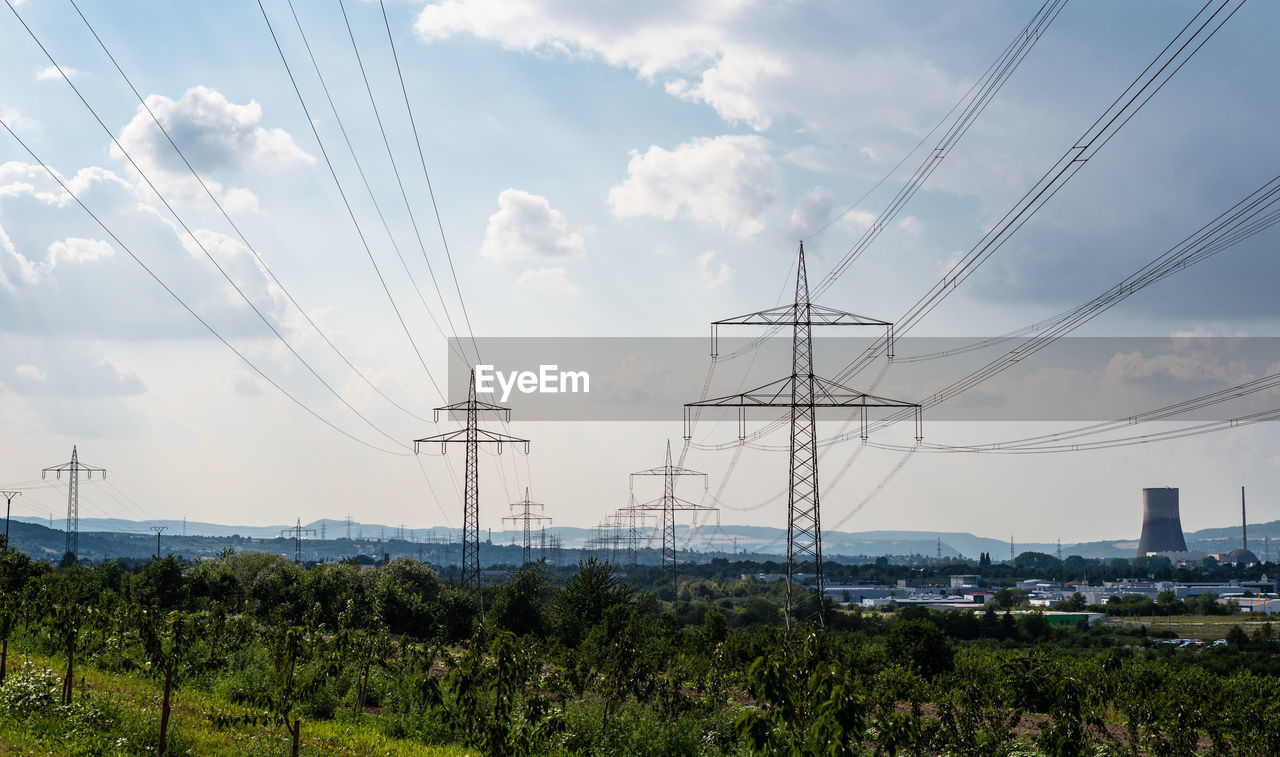 High voltage lines and power pylons in a green landscape, gray sky and chimney of a nuclear power 