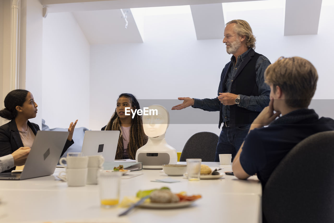 Business people discussing robot voice assistant during meeting