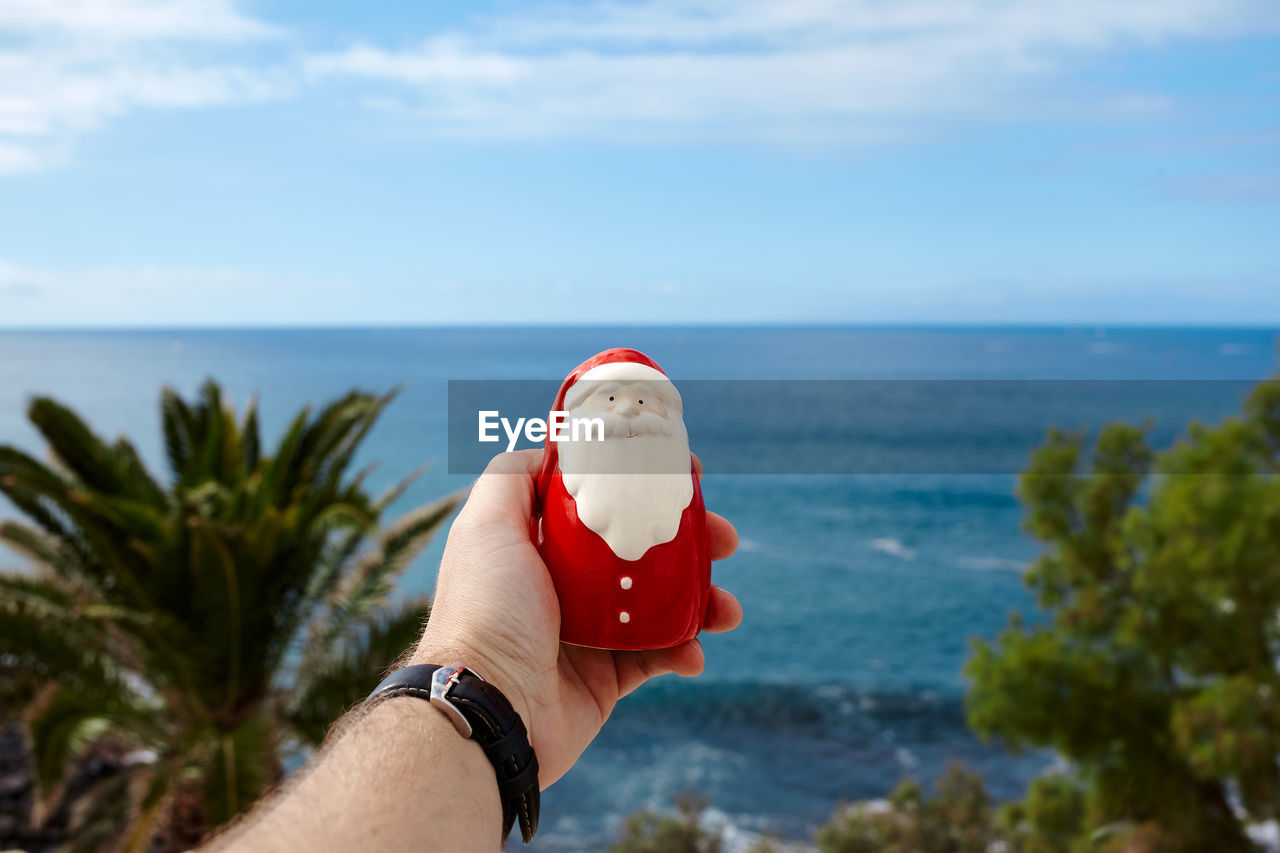 cropped hand of woman holding drink against sky