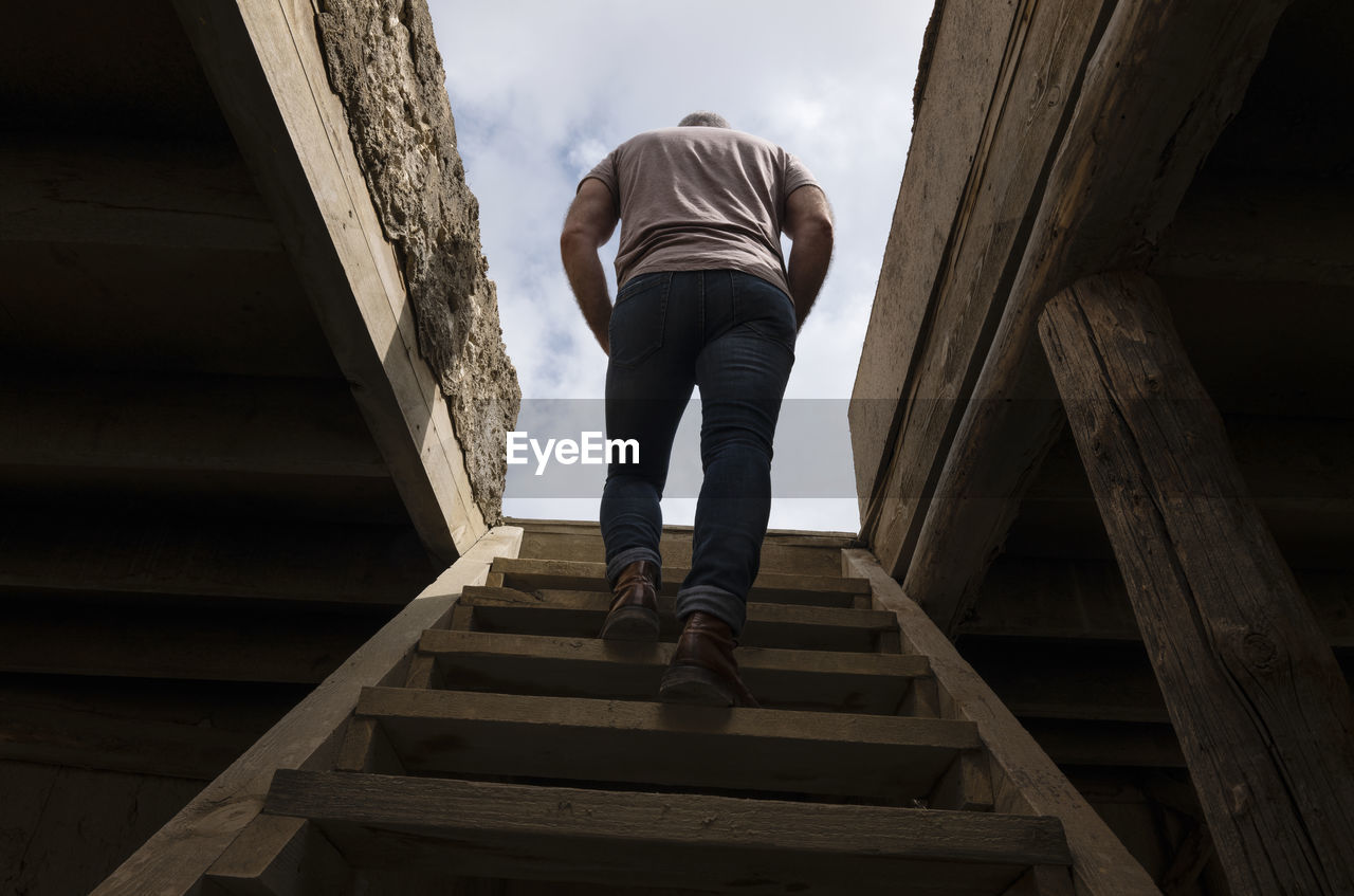 Rear view of adult man climbing up the wooden stairs, indoor toward the rooftop