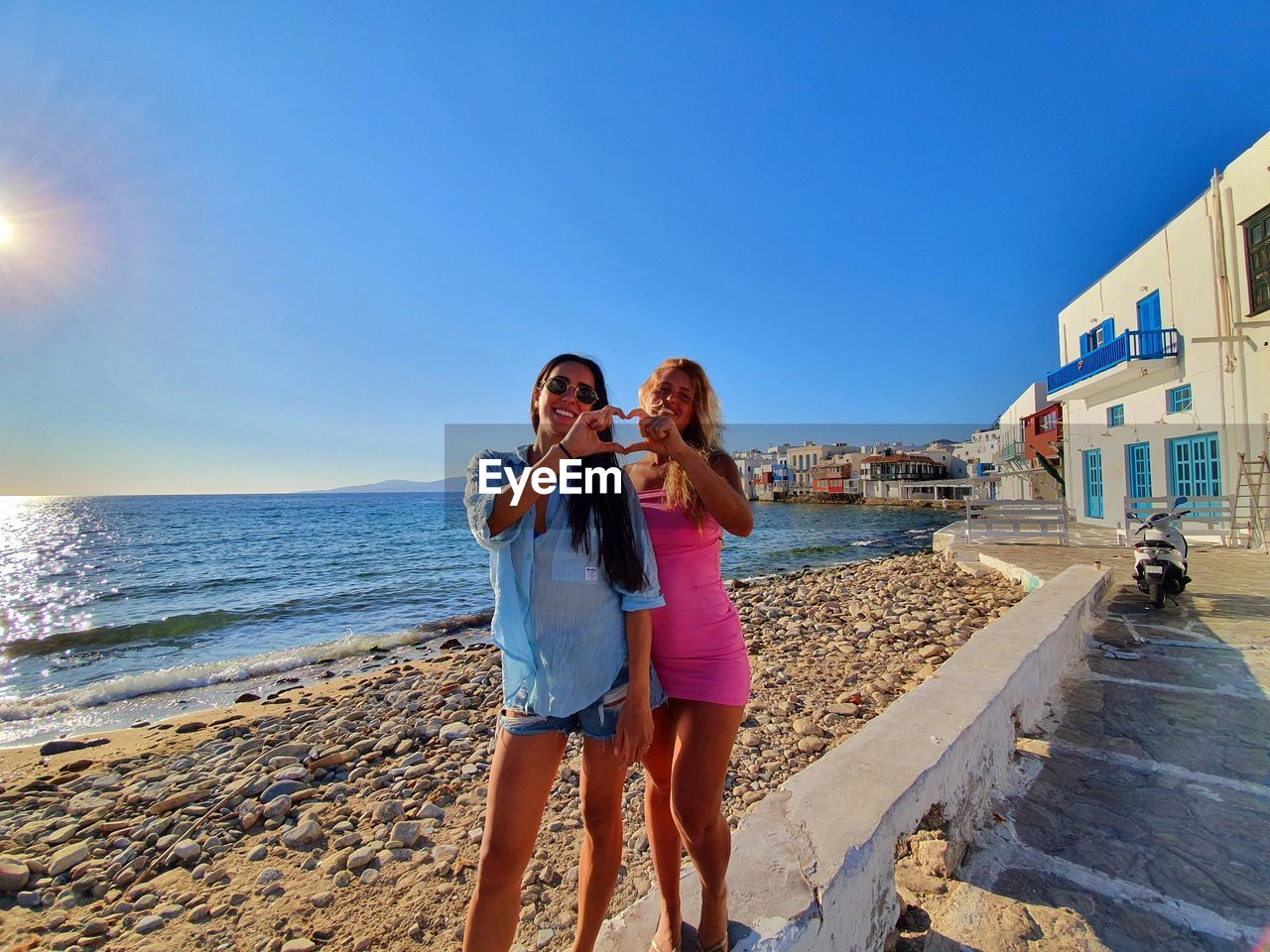 Women couple standing at beach against blue sky