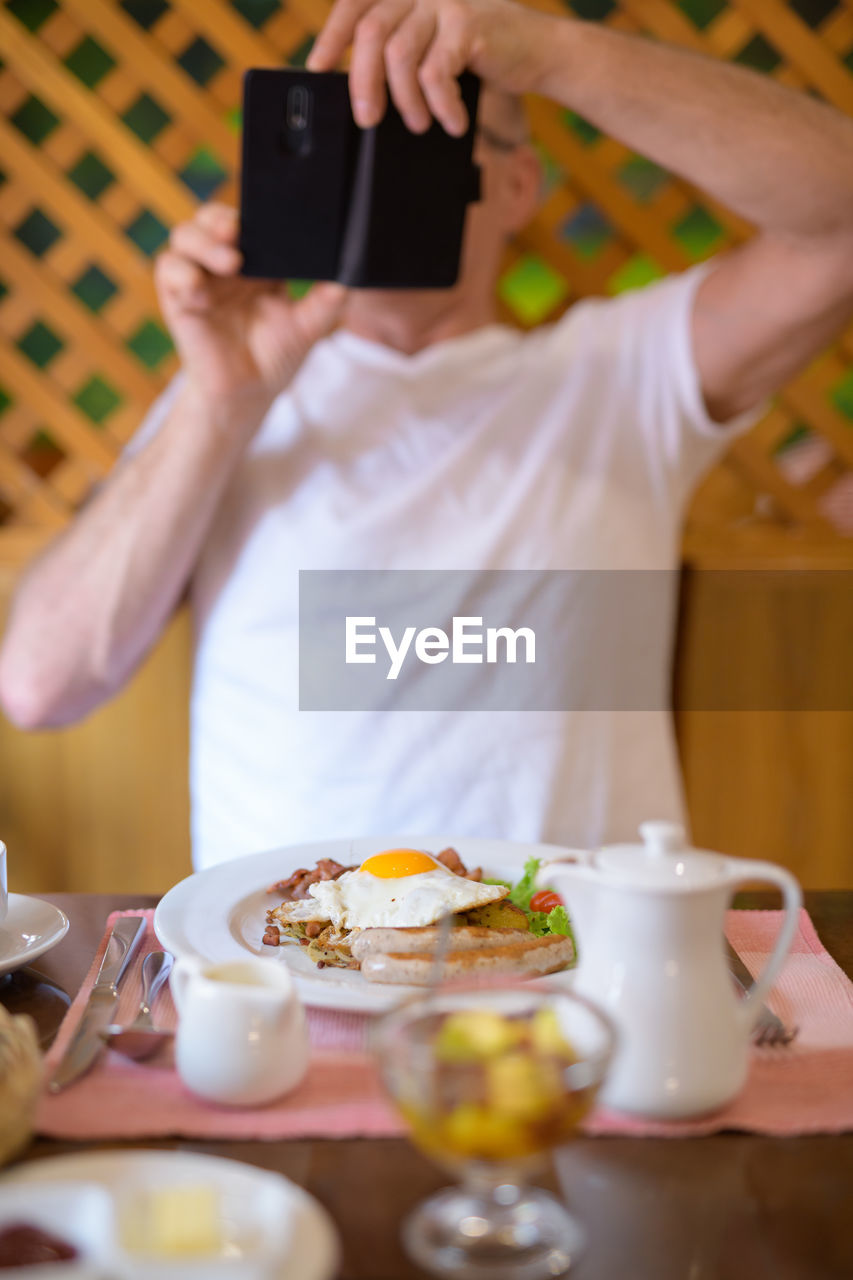 Man photographing food on table with mobile phone