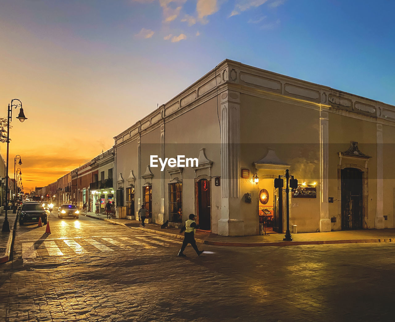 ILLUMINATED STREET BY BUILDING AGAINST SKY AT SUNSET