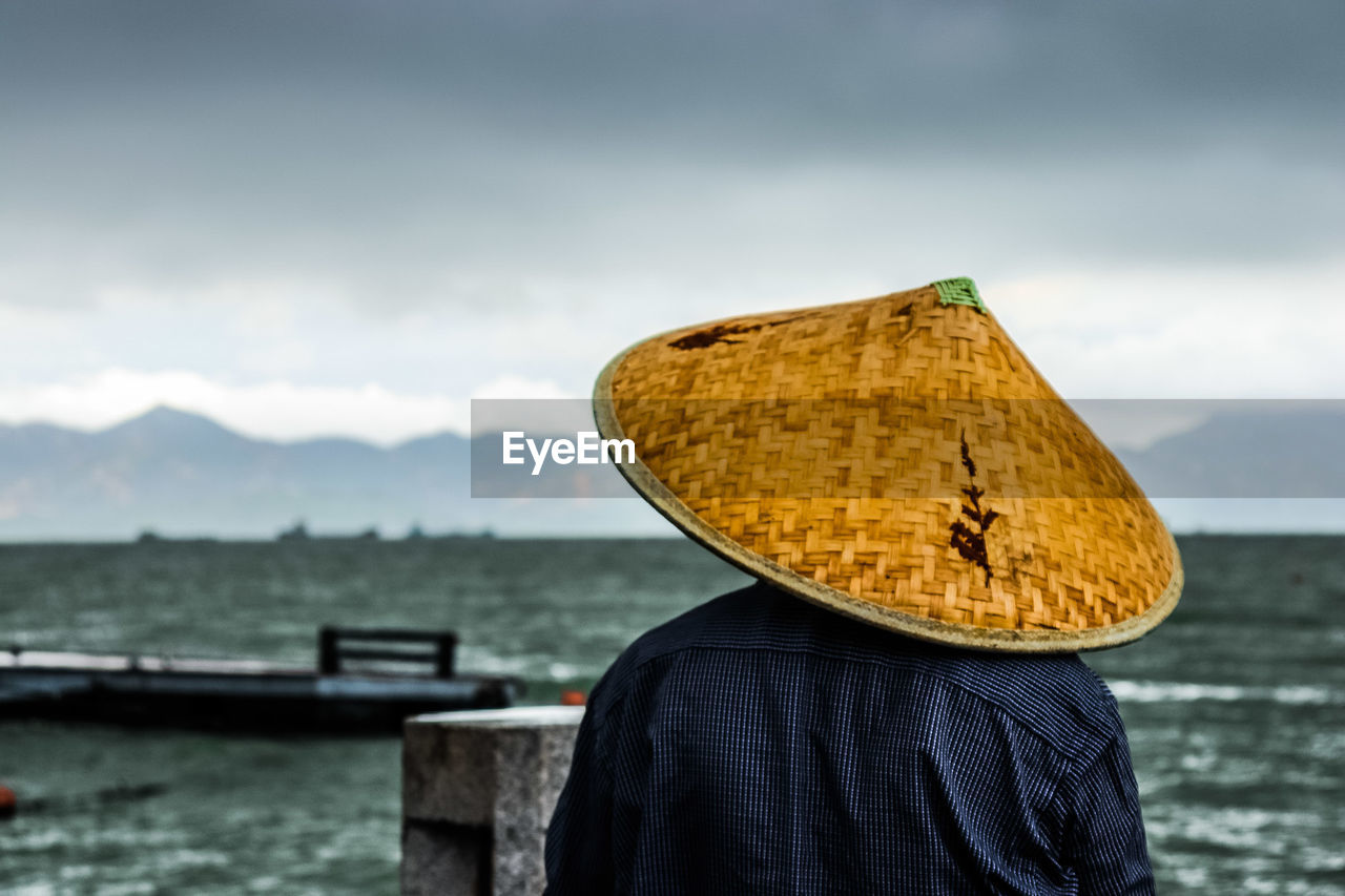 Rear view of men wearing asian style conical hat at beach against sky