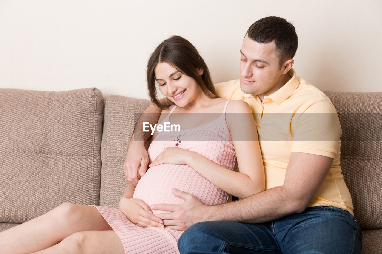 Happy pregnant woman and her husband waiting for baby at the home. happy family love and care.