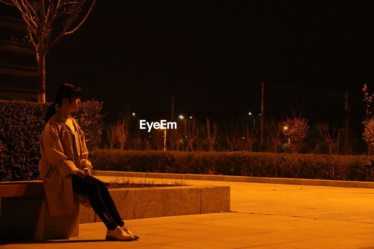 Young woman looking away while sitting in park at night