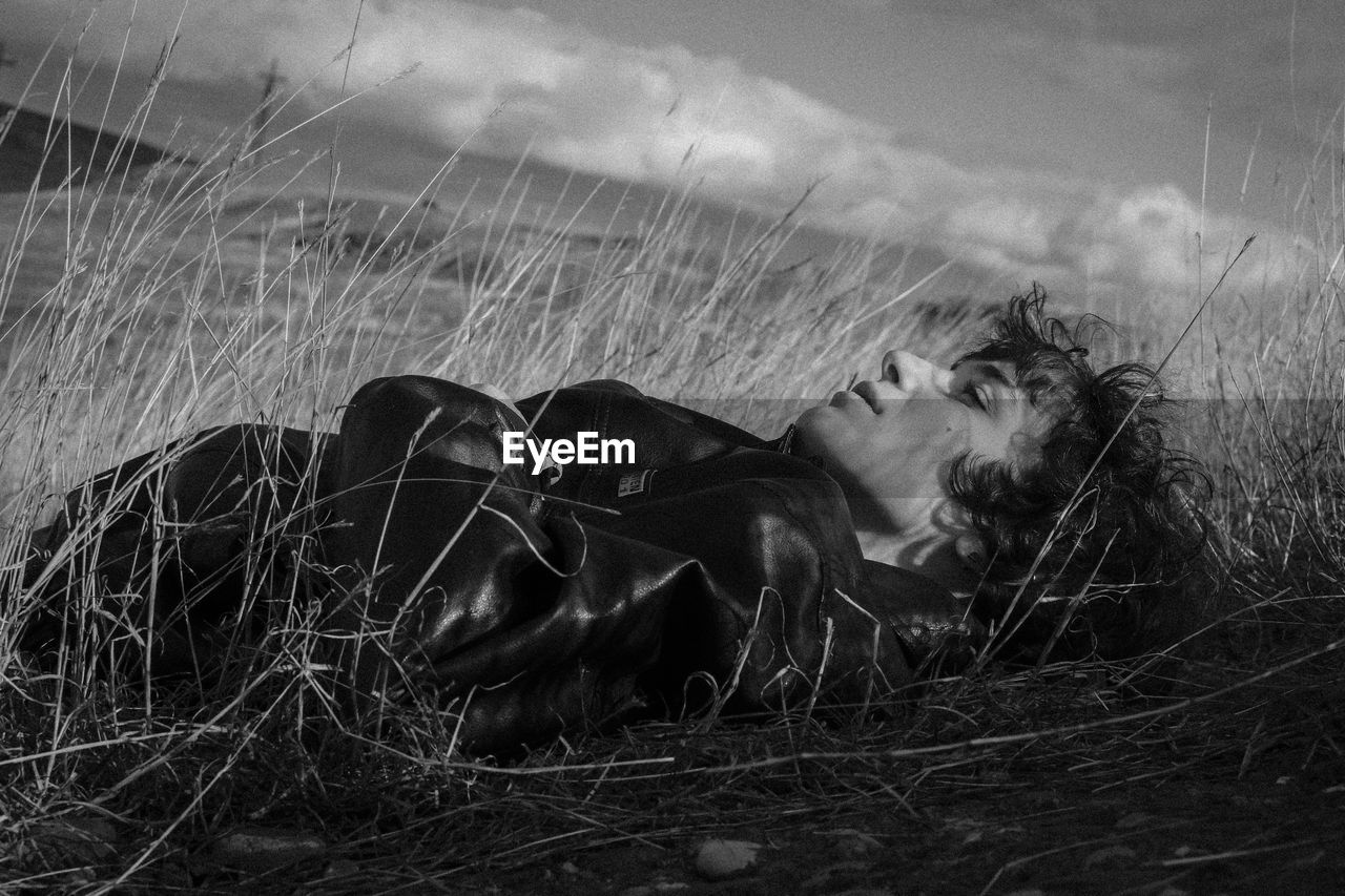 Young woman lying on field against sky