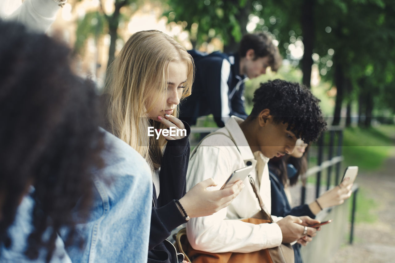 Male and female friends using smart phones in park